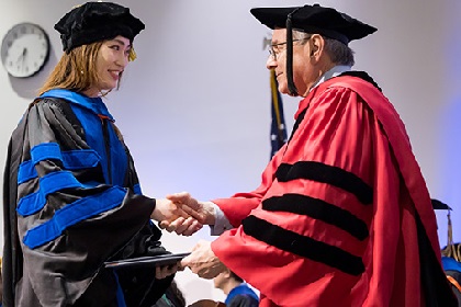 Young asian woman in black cap and gown accept diploma from Dr. Podolsky at UT Southwestern